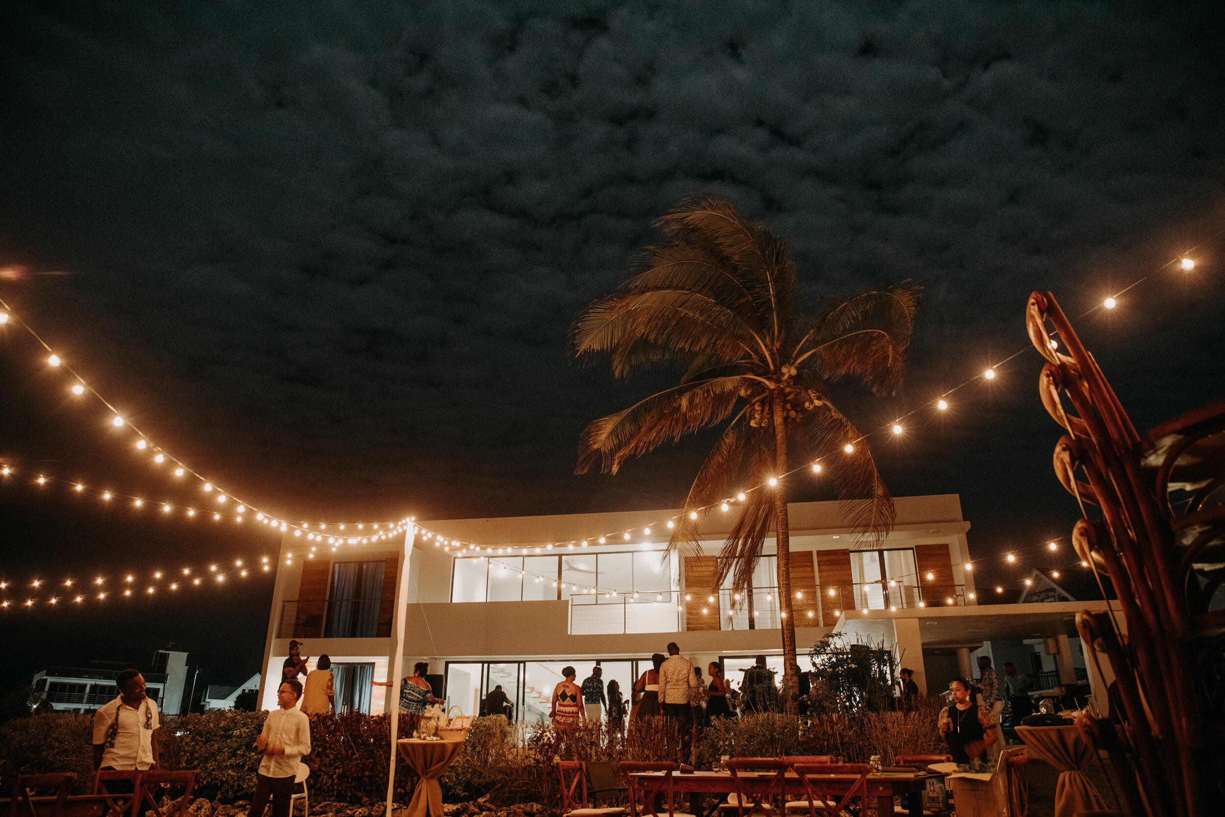 bright string lights shine against the dark cloudy night sky as wedding guests mingle